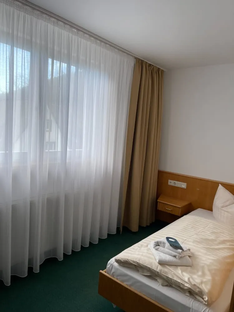 Einfach eingerichtetes Hotelzimmer mit Bett, Nachttisch und großem Fenster.